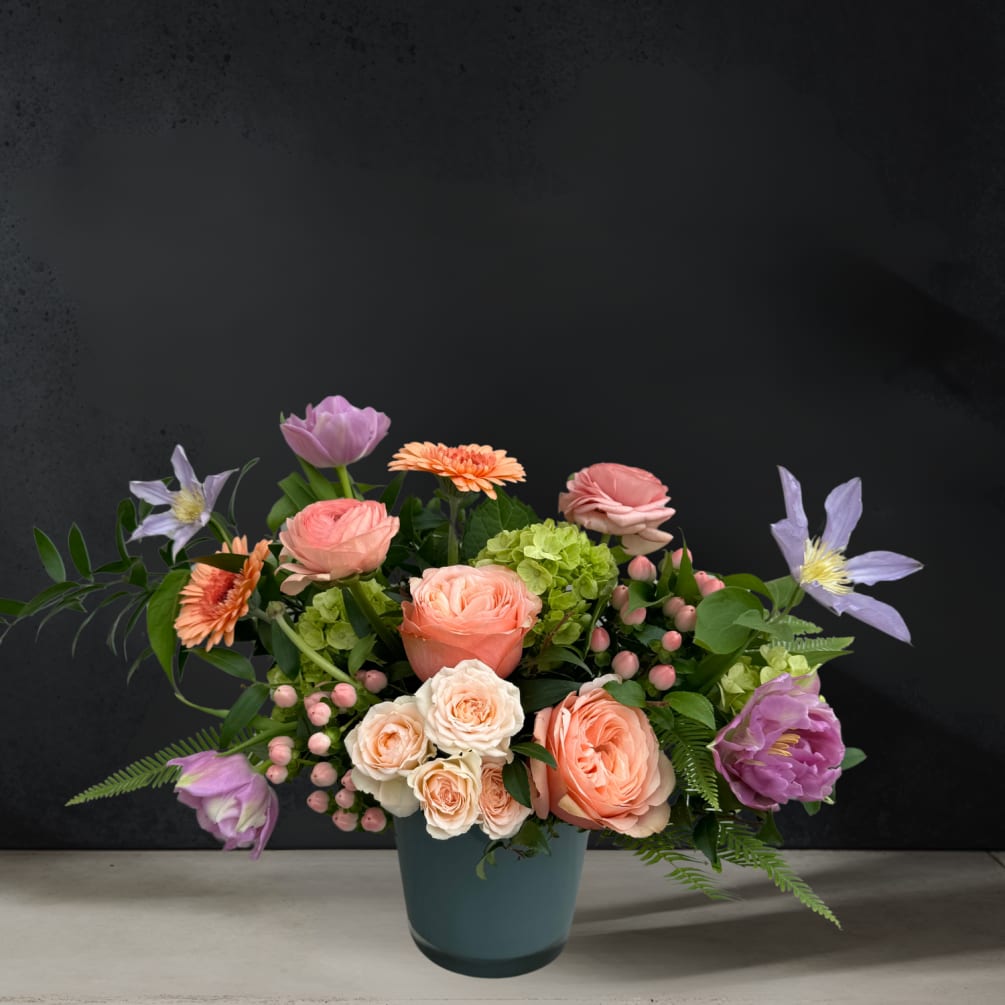 A sleek gray glass vase cradles a one-sided arrangement of soft peach