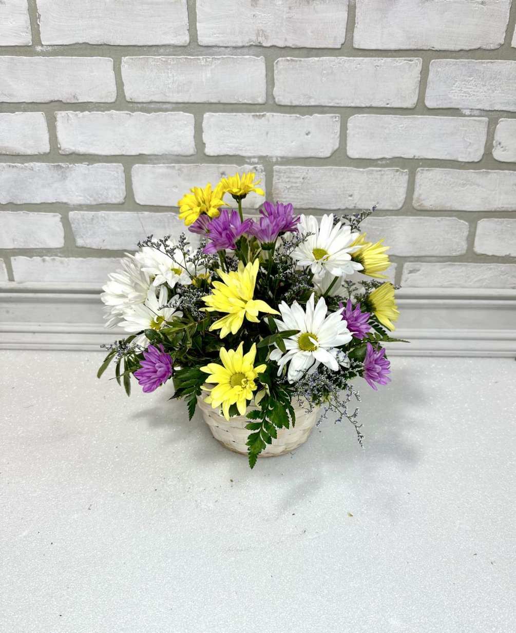 A traditional white basket filled with daisies and alstroemeria lilies. *Colors may