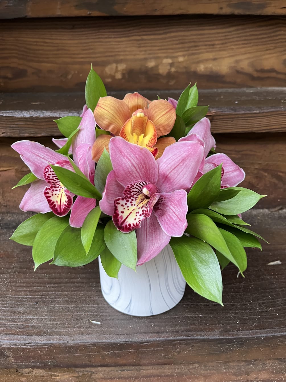 5-6 Cymbidium Orchids and hearty greens is a marble vase.  Orchid