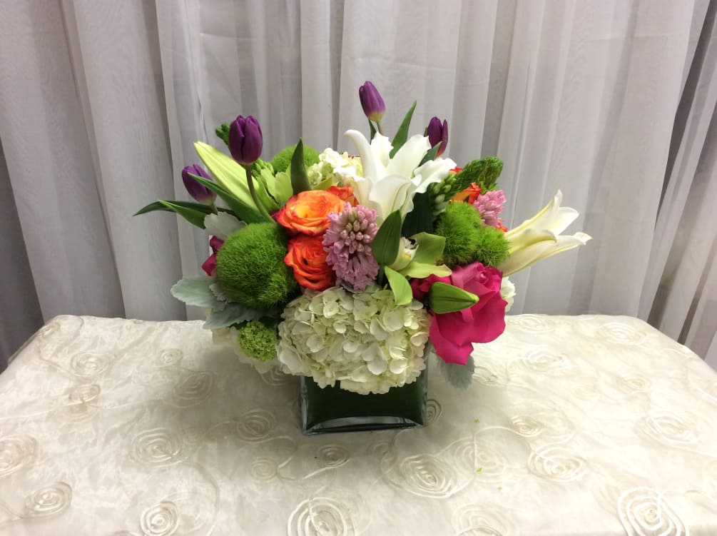Roses, tulips, lilies, hydrangea, dianthus, and hyacinth in a square glass vase.