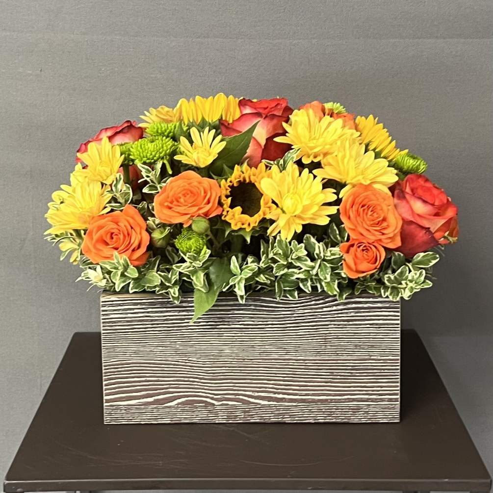 This floral arrangement is designed in a wood box using seasonal flowers.