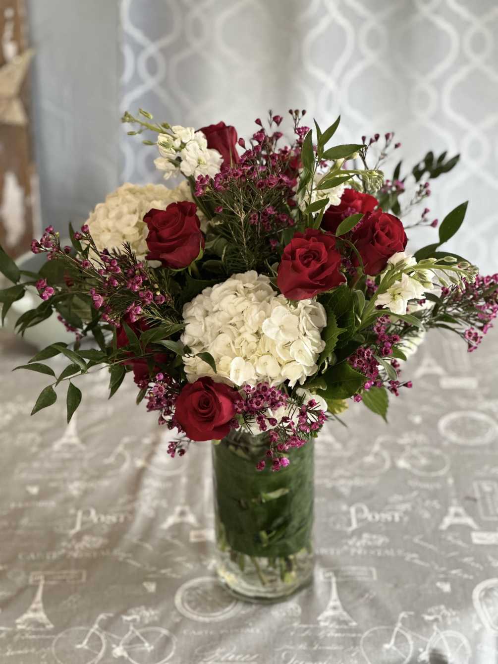 1 dozen roses arranged in a vase with fillers and white hydrangea