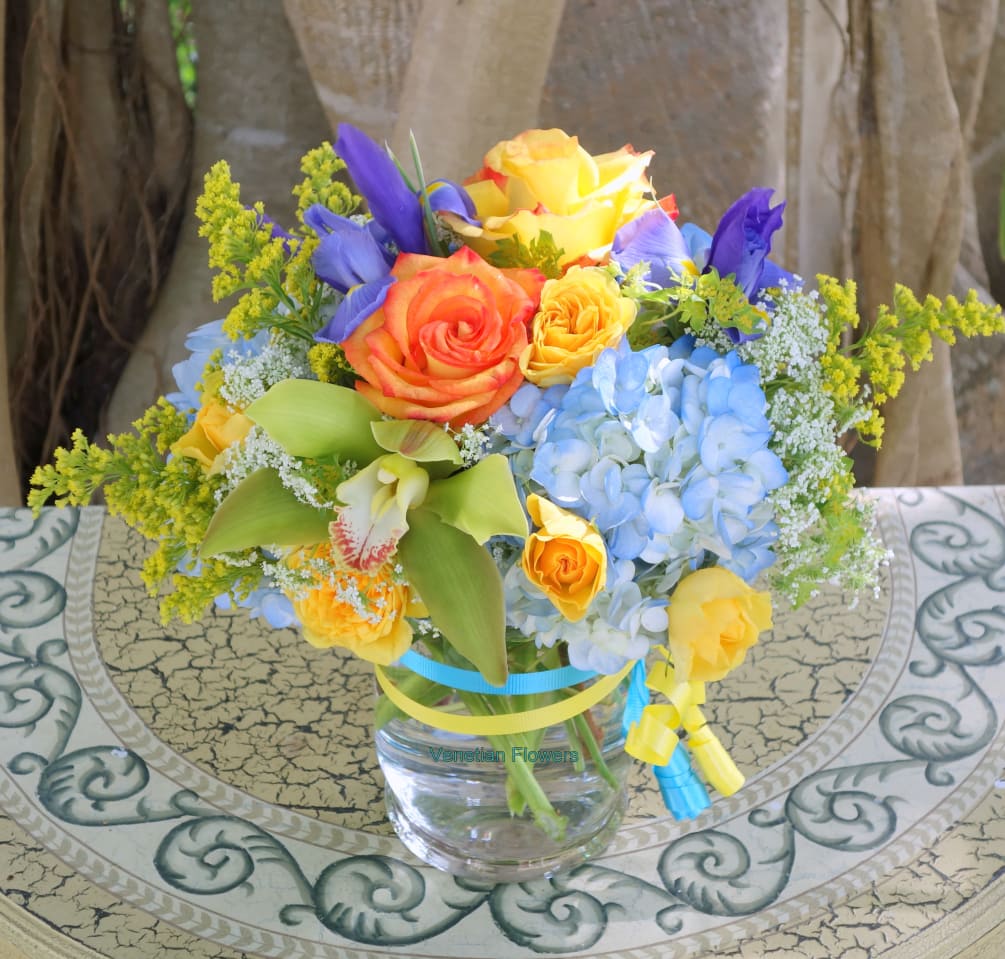 Arranged with Summer flowers including orange roses, yellow spray roses, blue hydrangeas