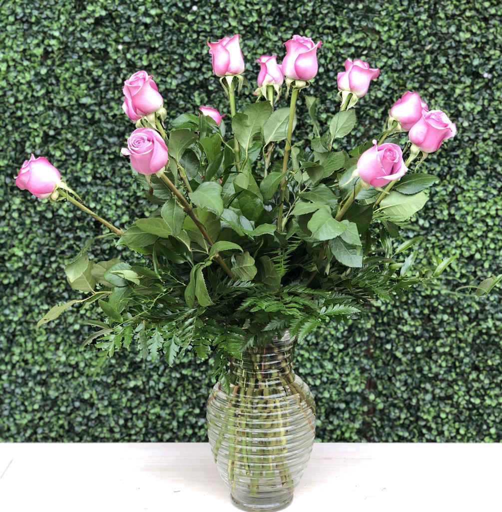 A traditional arrangement of lavender roses and greens in a glass vase.