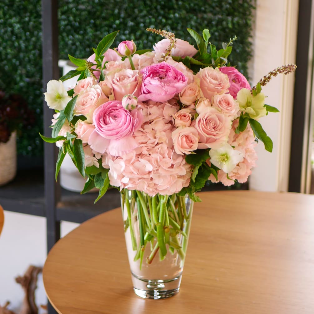 This ethereal arrangement features a soft, pale pink palette of roses, ranunculus