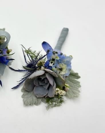 A boutonniere featuring blue toned succulents, belladonna and blue-gray ribbon.

Depending on availability