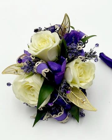 A wrist corsage featuring white spray roses, dark purple larkspur, purple filler