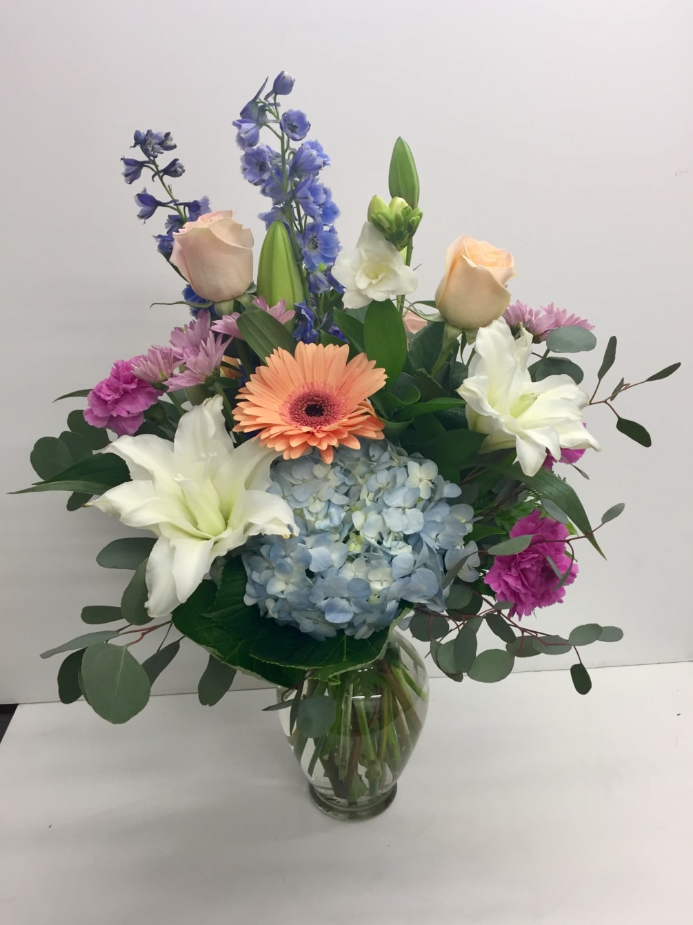 Vase of peach gerbera daisies, roses, lilies and blue hydrangea