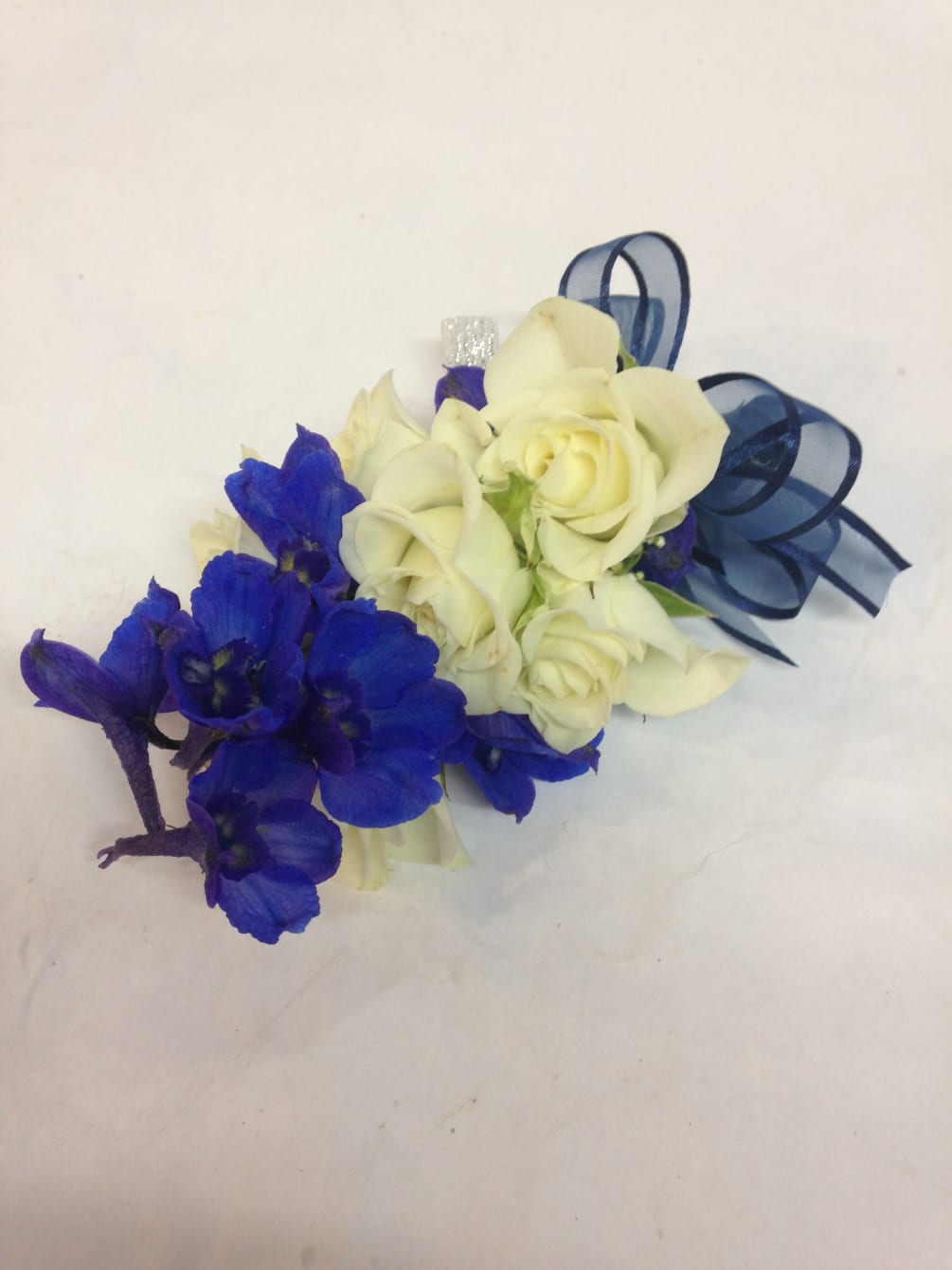 This modern corsage features crisp blue delphinium paired with white spray roses.