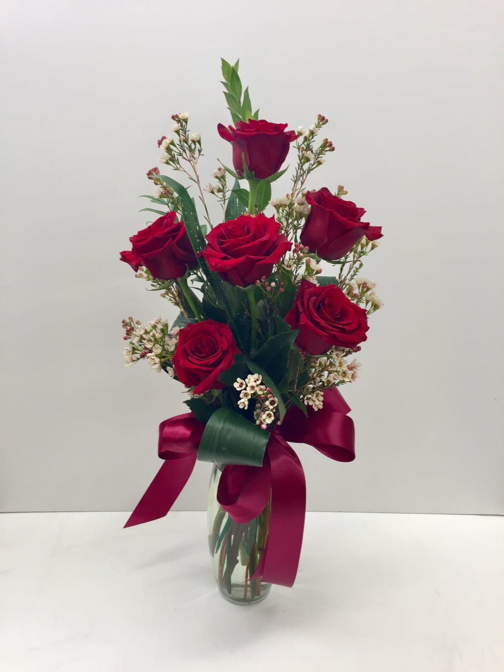 Half dozen velvet explorer roses in vase with accent flowers and foliages