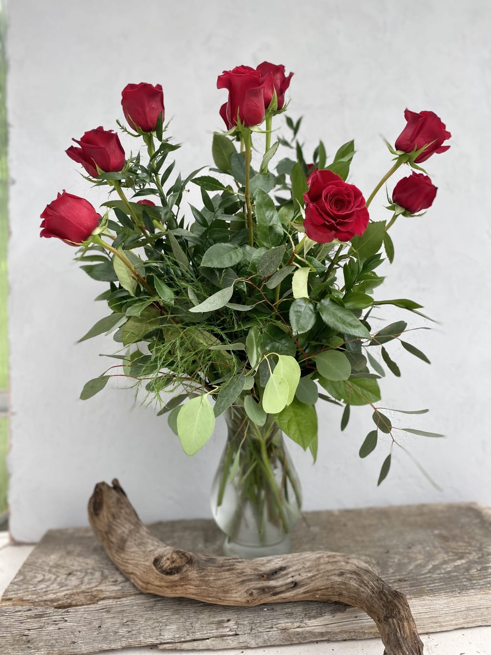 A dozen roses with mixed green filler in a tall glass vase.