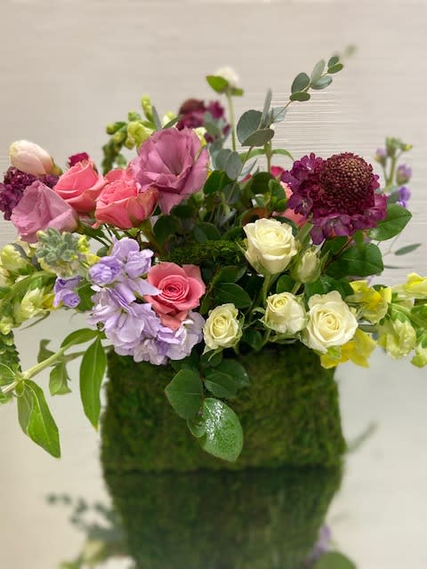 A mossed basket with handles filled with fresh seasonal blooms.