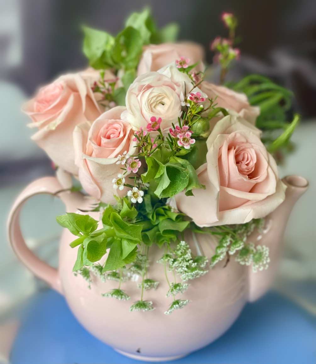 An adorable tea pot filled with blush roses greenery and pink ranunculus