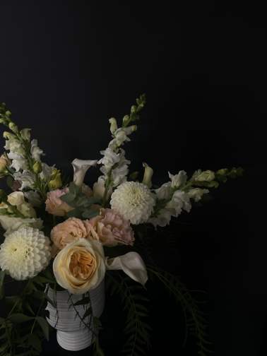 Soft peach and white flowers arranged in a white vase against a dark background.