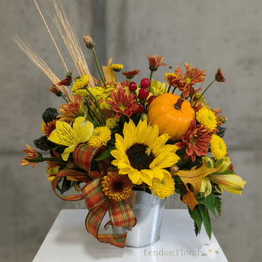 Fall floral arrangement with sunflowers, mums, and a small pumpkin in a metal bucket