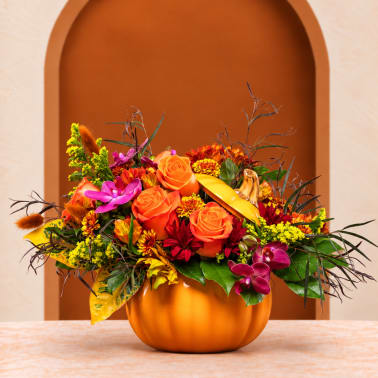Orange and purple floral arrangement in a pumpkin-shaped container
