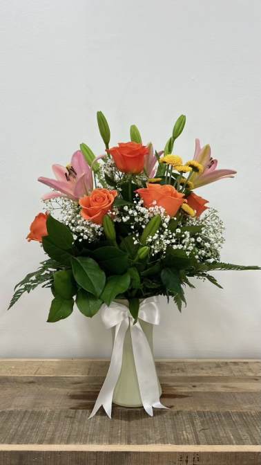 Orange roses and pink lilies in a white vase with a ribbon
