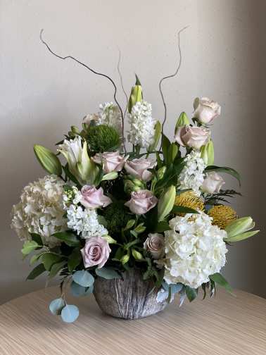 Arrangement of pale roses, white lilies, and hydrangeas in a rustic vase