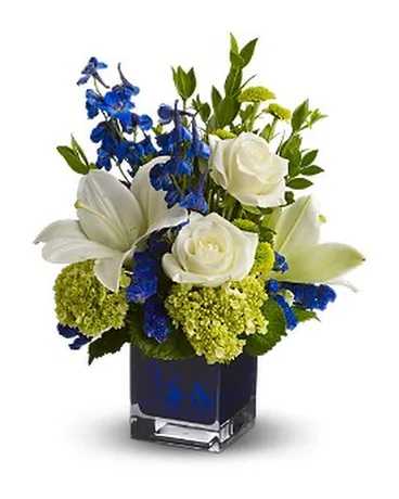 White lilies and roses with blue flowers in a square glass vase