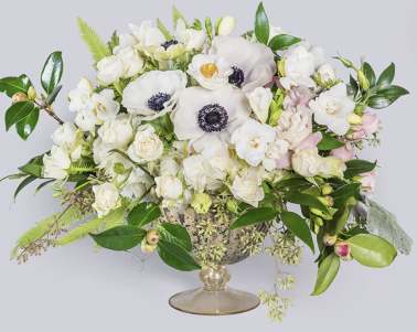White floral arrangement in a glass compote vase with pink accents