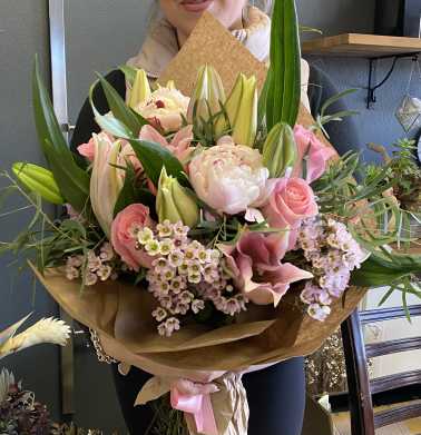 Large bouquet of pink roses, lilies, and peonies wrapped in brown paper
