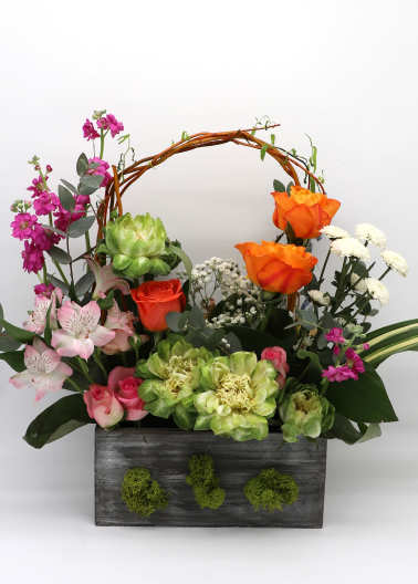 Mixed floral arrangement in a dark wooden box with an arched twig handle