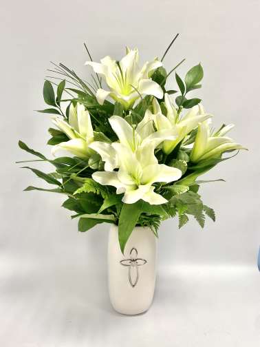 White lilies arranged in a white vase with green foliage