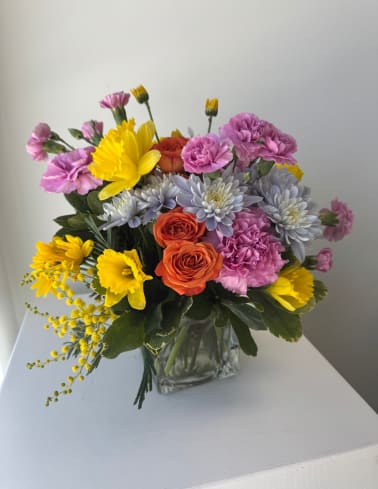 Mixed bouquet of yellow, pink, orange, and lavender flowers in a clear glass vase