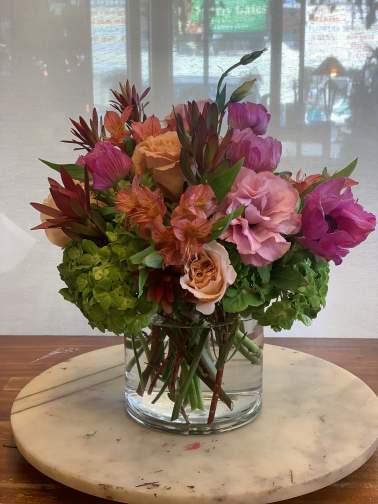 Mixed bouquet of pink, peach, and orange flowers in a clear glass vase