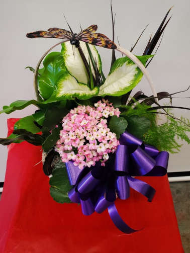 Basket arrangement with pink flowers, green-and-white leaves, and a butterfly topper