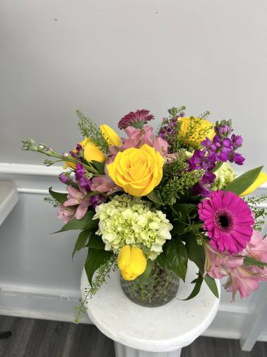 Mixed arrangement of yellow roses and tulips with pink and purple blooms in a clear glass vase