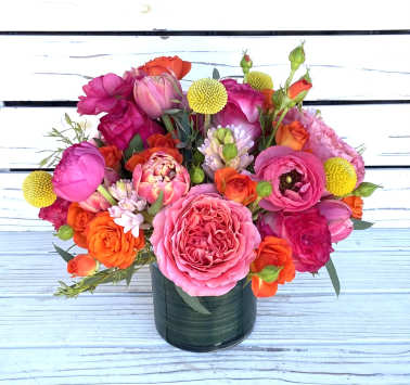 Bright arrangement of pink and orange roses, ranunculus, and tulips in a green glass vase