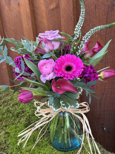 Pink and magenta bouquet in a blue glass vase with raffia bow