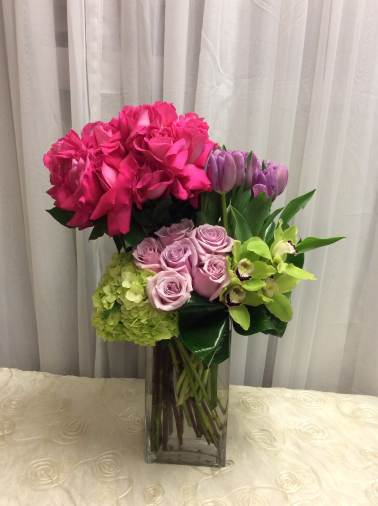 Pink roses, lavender roses, tulips, hydrangea, and green orchids in a glass vase