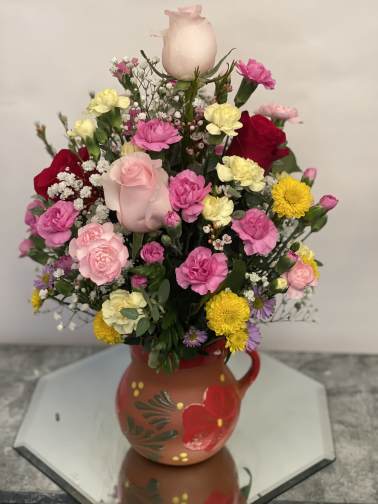 Mixed bouquet in a painted ceramic pitcher with pink, yellow, and red blooms