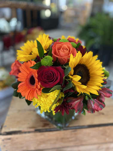Mixed bouquet of roses, sunflowers, and gerbera daisies in a glass vase