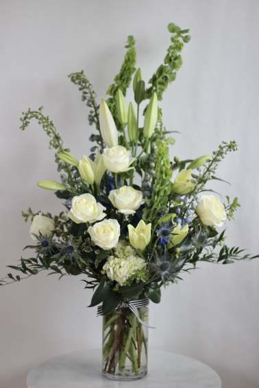 White roses and lilies in a tall glass vase with blue thistle accents