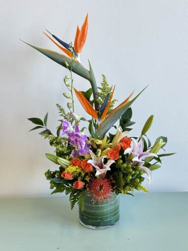 Tropical bouquet with orange bird of paradise and lilies in a glass vase