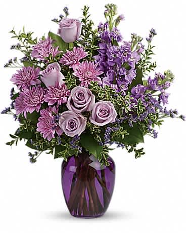 Purple and lavender roses, mums, and stock arranged in a purple glass vase.