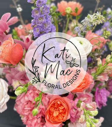 Mixed bouquet of pink, peach, and purple flowers with roses and delphinium, with a circular florist logo overlay.