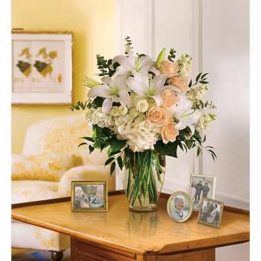 White lilies and peach roses arranged in a glass vase on a table