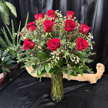 Red roses arranged in a clear glass vase with small white filler flowers