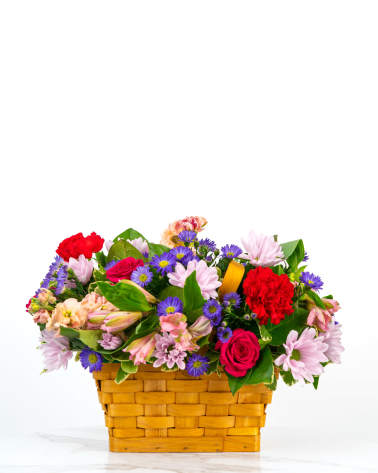 Low basket arrangement of pink daisies, red roses, red carnations, and purple asters in a woven wood basket