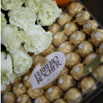 White roses beside gold-wrapped Ferrero Rocher chocolates in a gift box