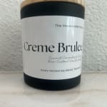 Black candle jar with a wood lid labeled Creme Brulee
