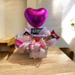 Heart-shaped pink balloon above a candy gift basket with a pink bow