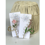 Two floral hair clips on branded cards beside a woven straw hat