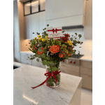 Orange roses and yellow blooms in a glass vase with a red ribbon