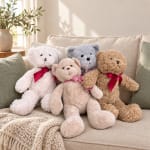 Three teddy bears with ribbon bows sitting on a beige sofa