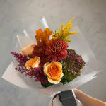Bouquet of orange roses, burgundy mums, and purple hydrangea in white wrap